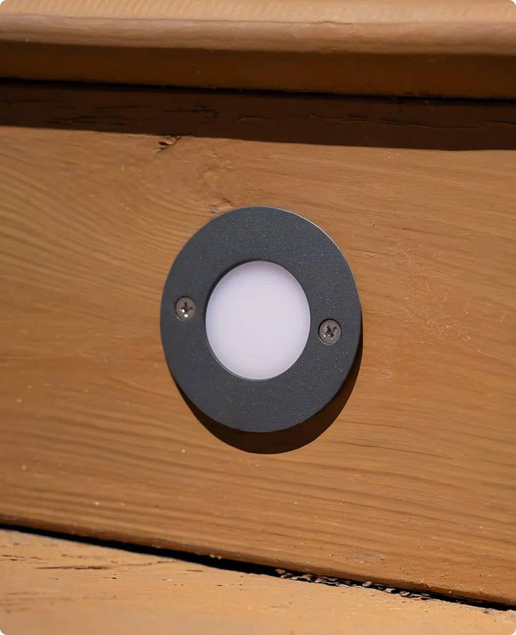 Close-up of a Gemstone deck light with a frosted cap in a dark metal ring set into a cedar board