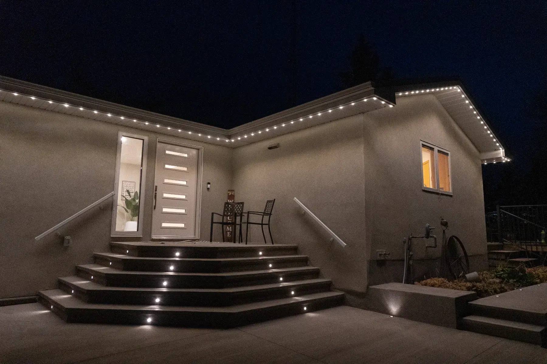 Back steps of a stucco home with warm white deck and roofline lights