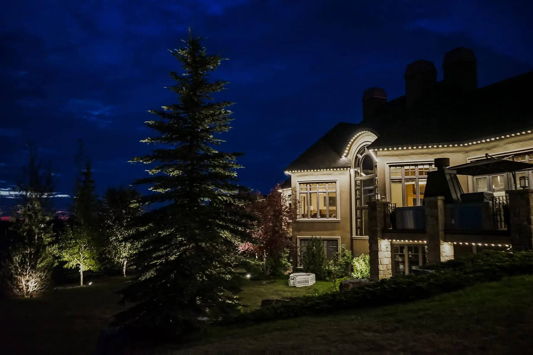 Large lodge with spruce trees uplit in warm white