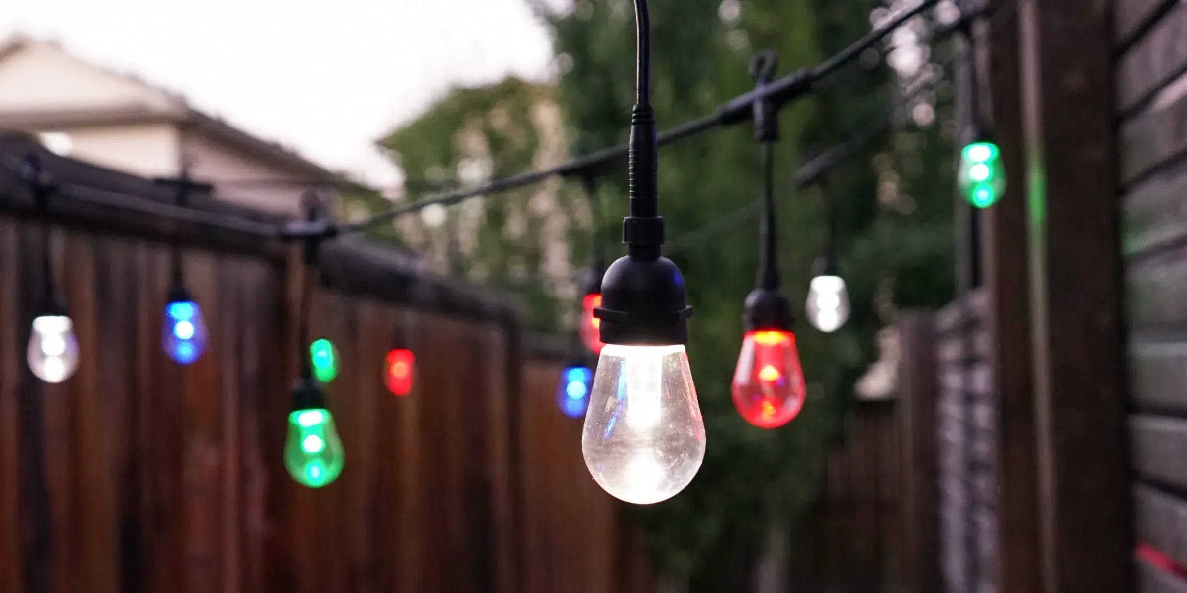 Gemstone patio string lights in several colours along a backyard fence