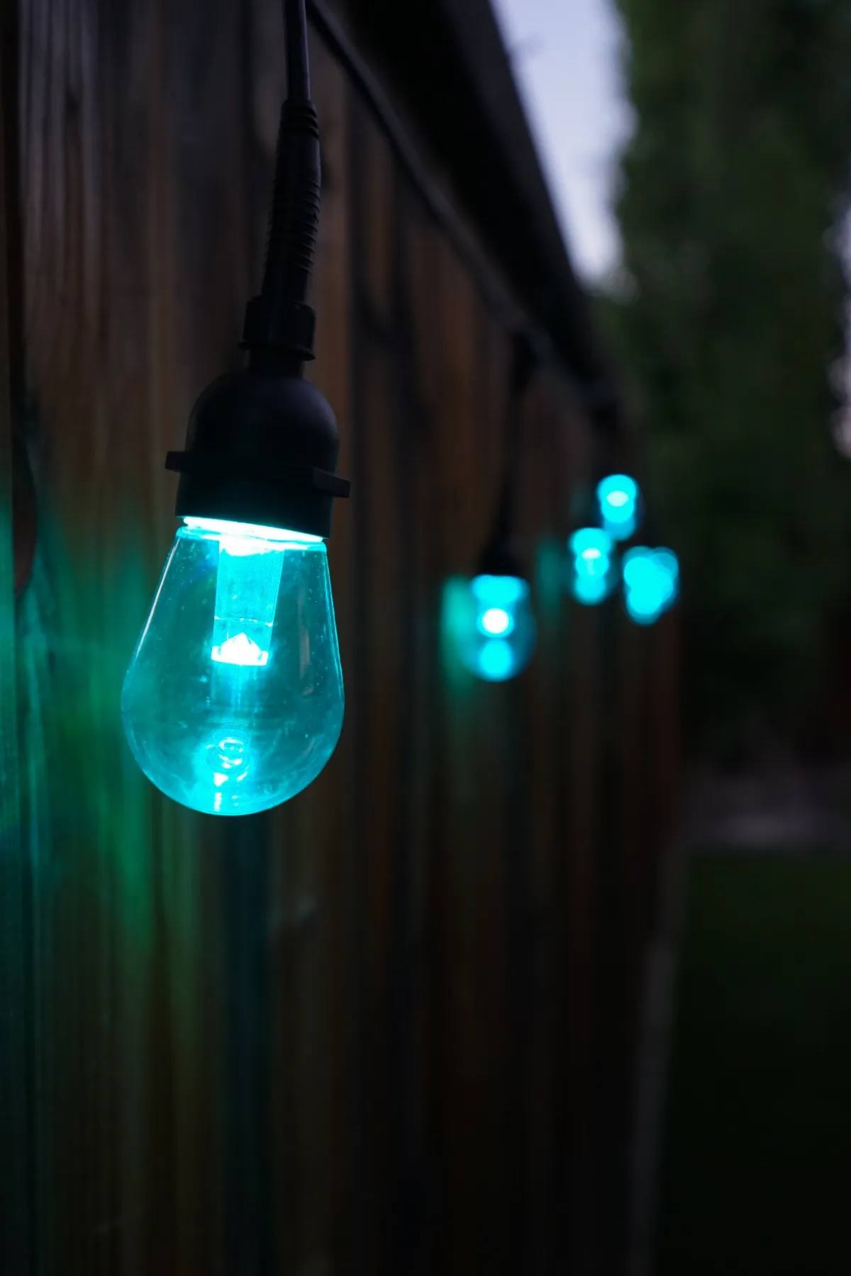 Teal Gemstone patio bulb glowing at dusk