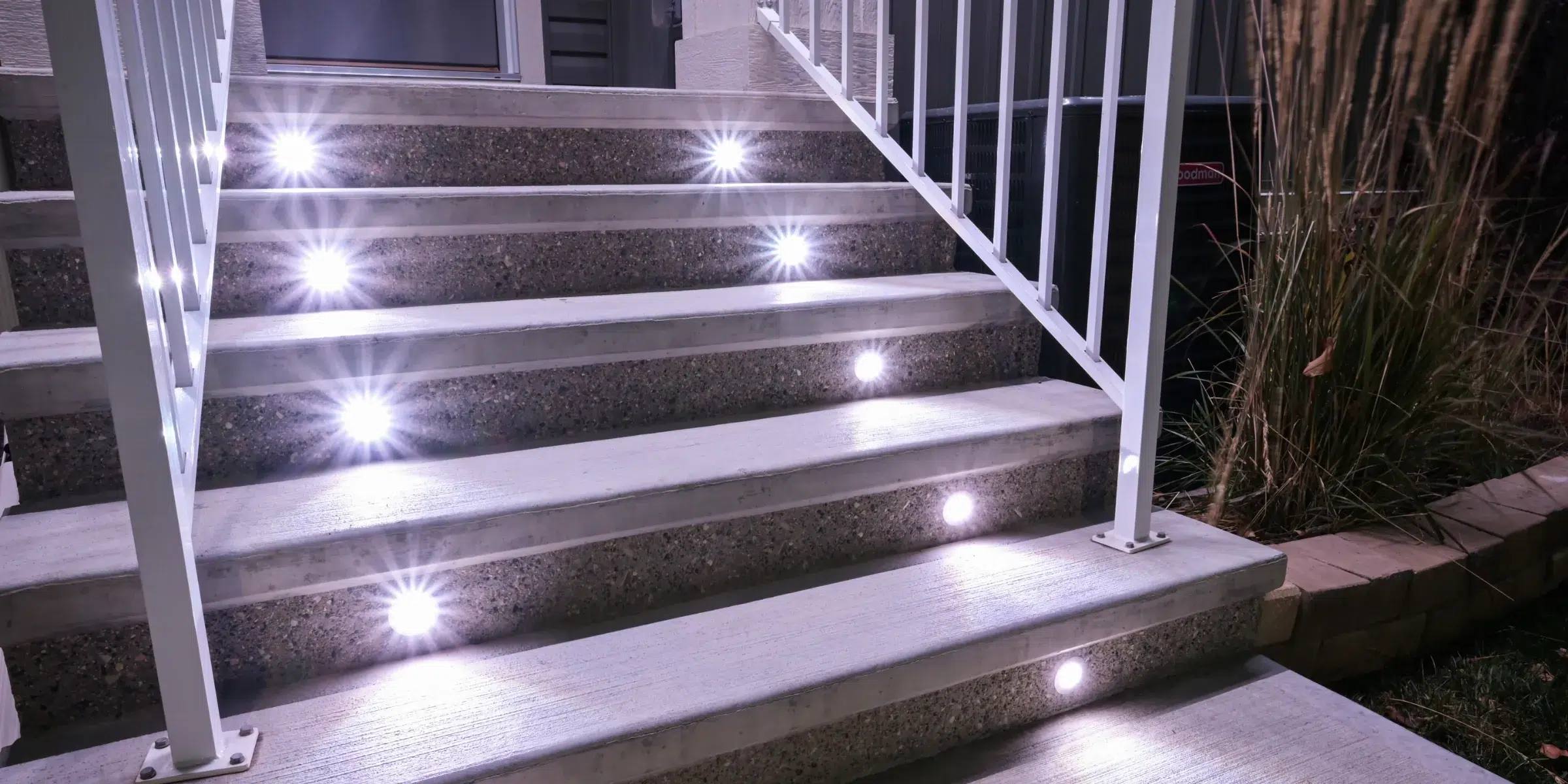 Concrete steps with bright white Gemstone deck lights beside a white railing